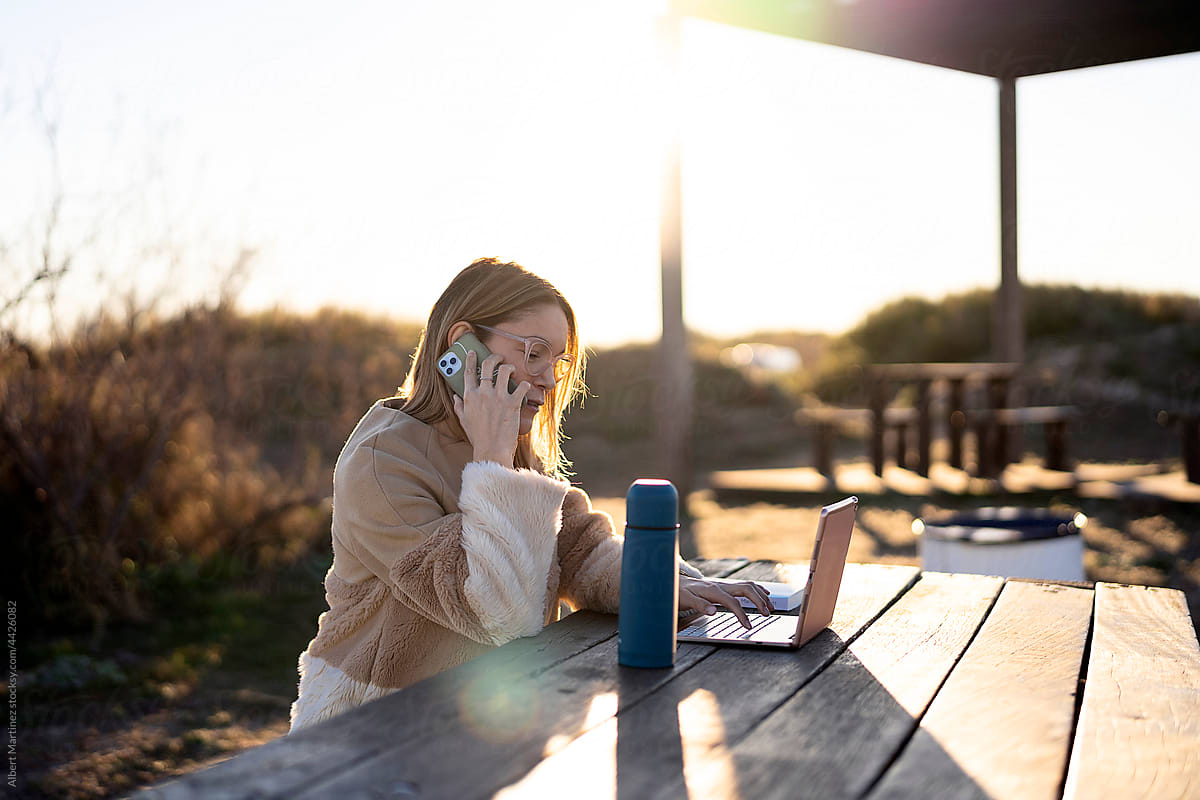 Woman browsing laptop while having phone call in countryside