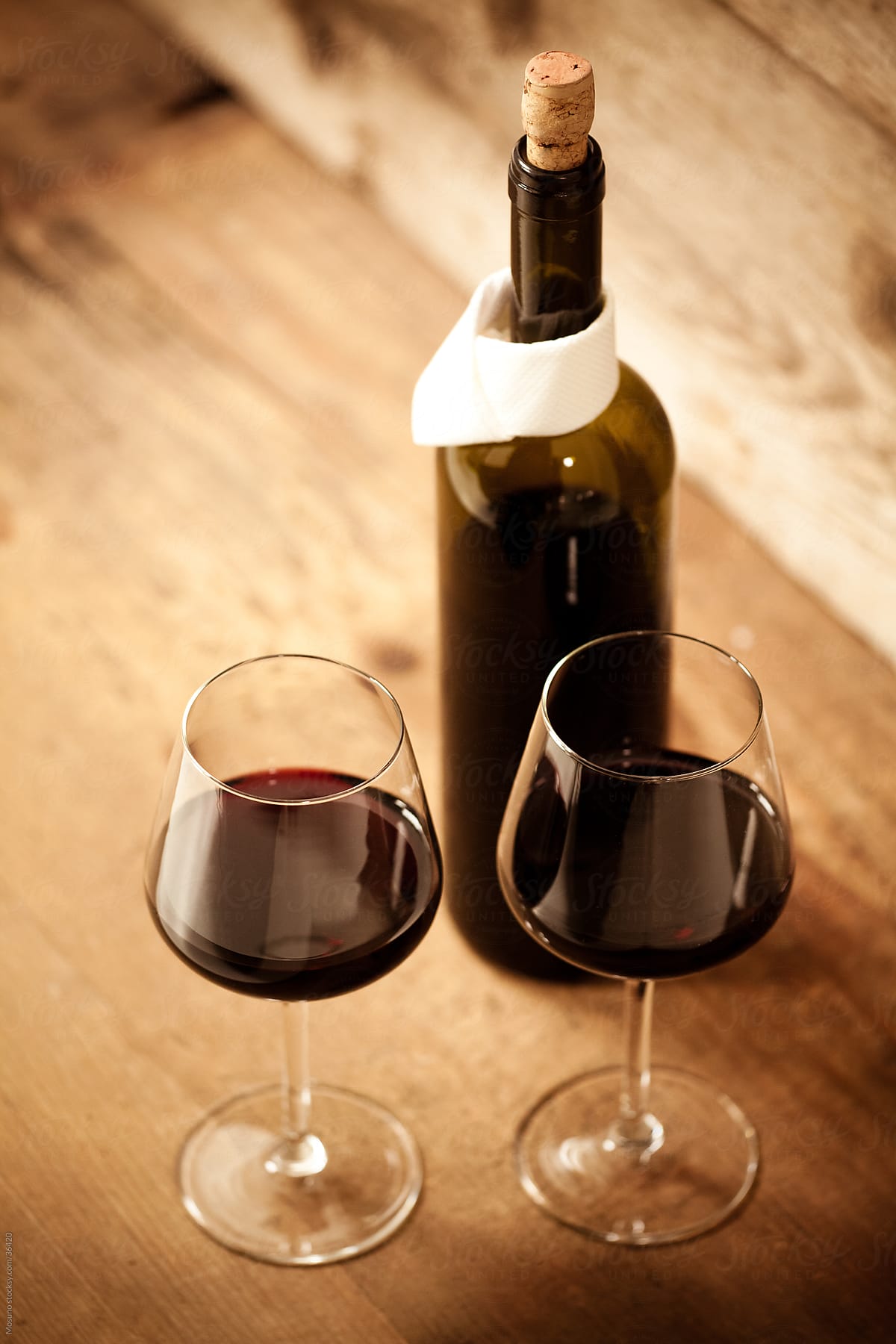 Two glasses of wine and a bottle on a wooden table.