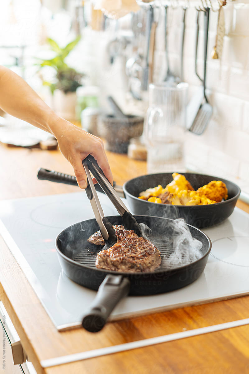 Person flipping steak with tongs on grill pan
