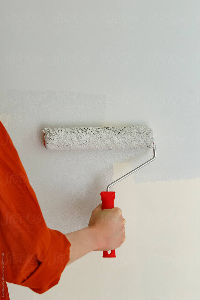 Crop person painting wall with roller