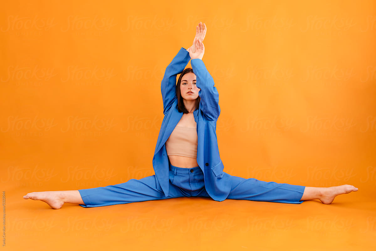 Young woman stretching legs on floor with orange wall
