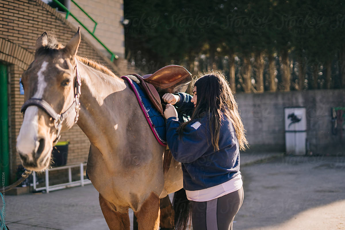 Brunette putting saddle on brown horse