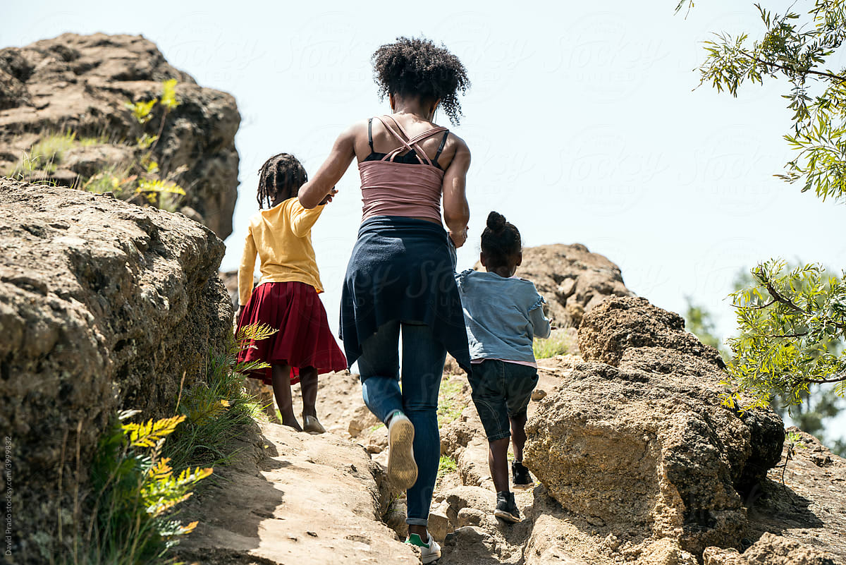Crop black family group climbing on rocky path in woods with children