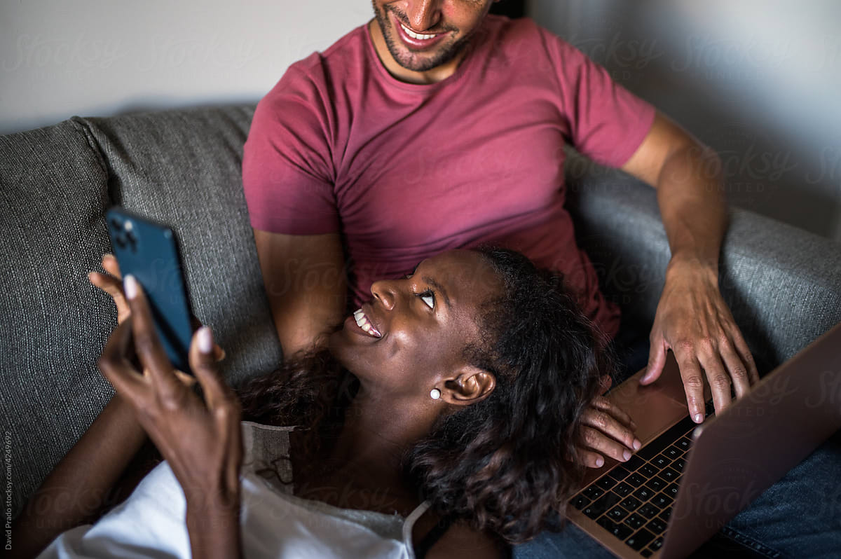 Multiracial couple using devices on couch