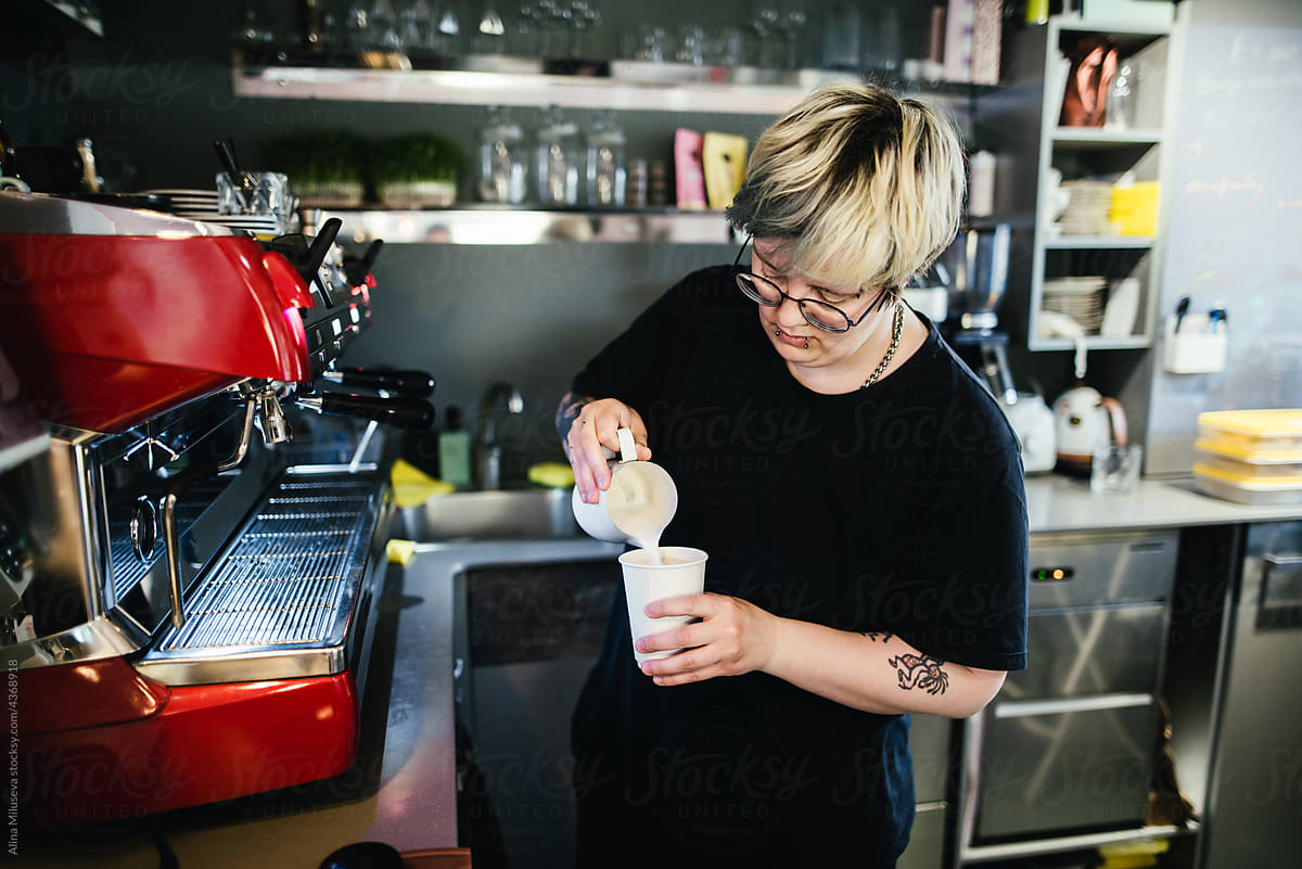 Woman barista pouring milk into a coffee cup