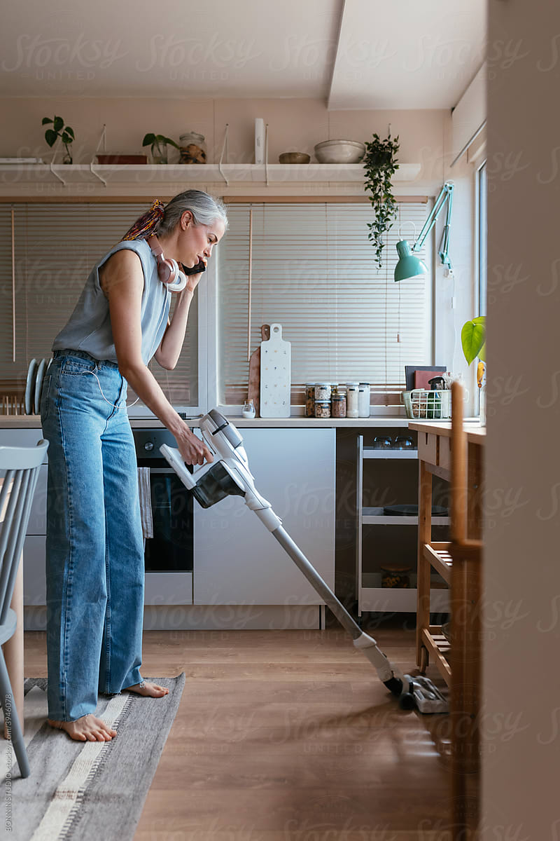 Mature woman cleaning kitchen and talking on smartphone