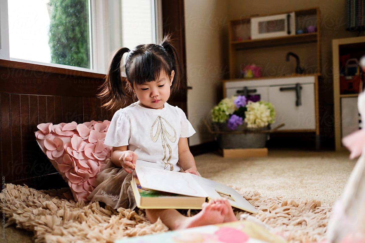 Asian Toddler Girl Reading A Book At Home by Take A Pix Media - Child, Cute