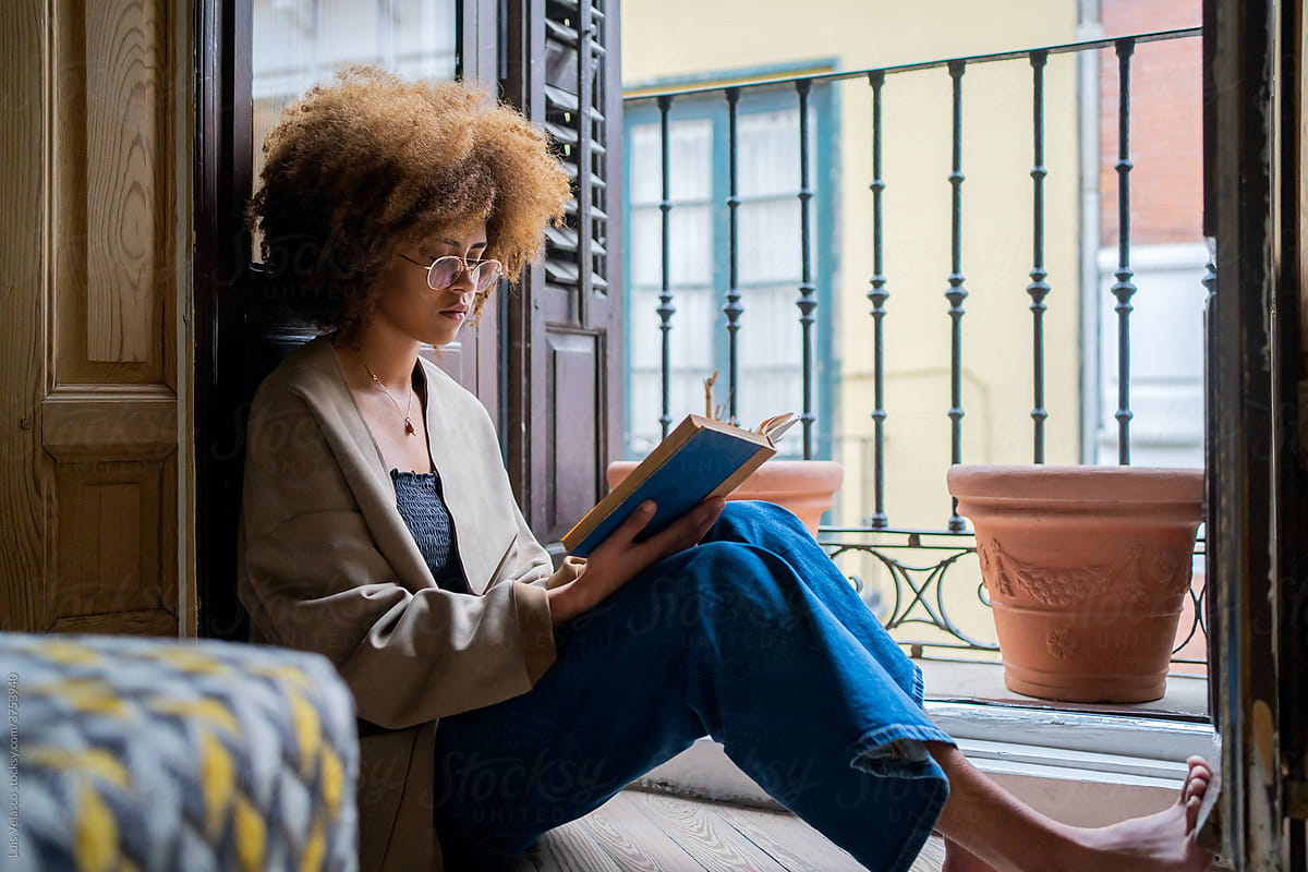 Black Woman Reading A Book Next To The Window.