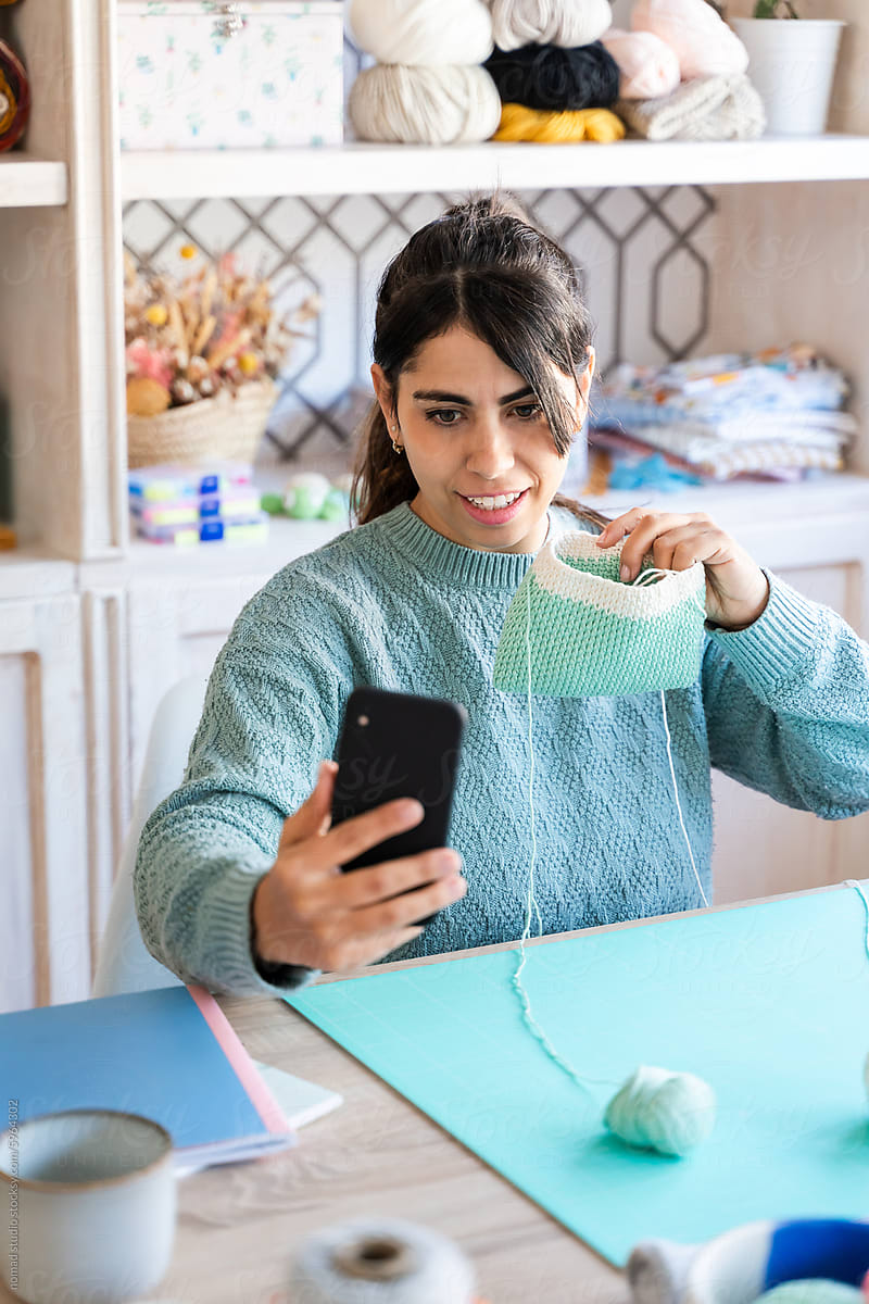 Young woman sharing knitting project on smartphone