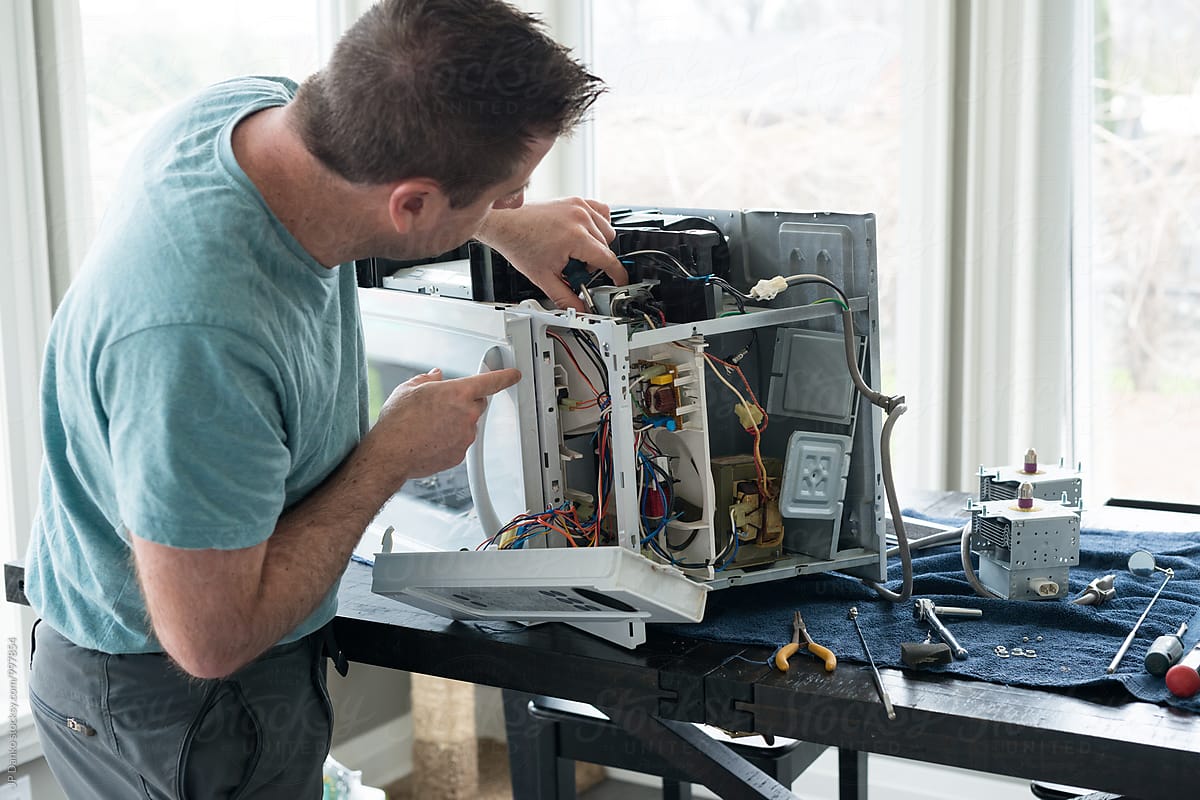 Repair Man Repairing Broken Microwave Oven In Kitchen