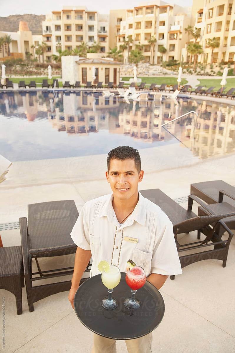 Portrait of server holding cocktails poolside at resort