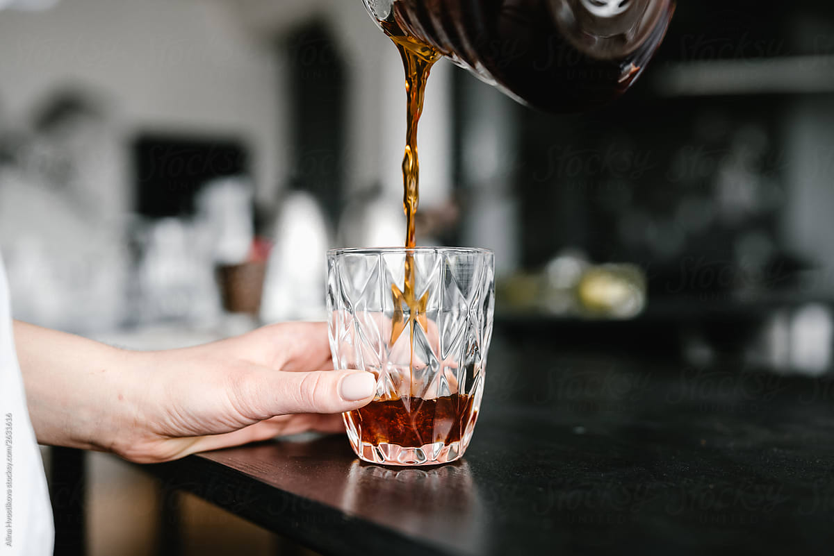 Barista pouring black coffee in glass.