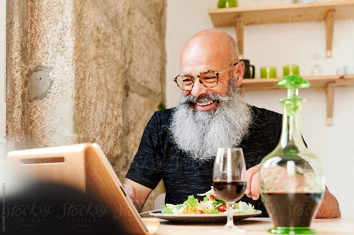 Laughing mature man using a tablet at dinner