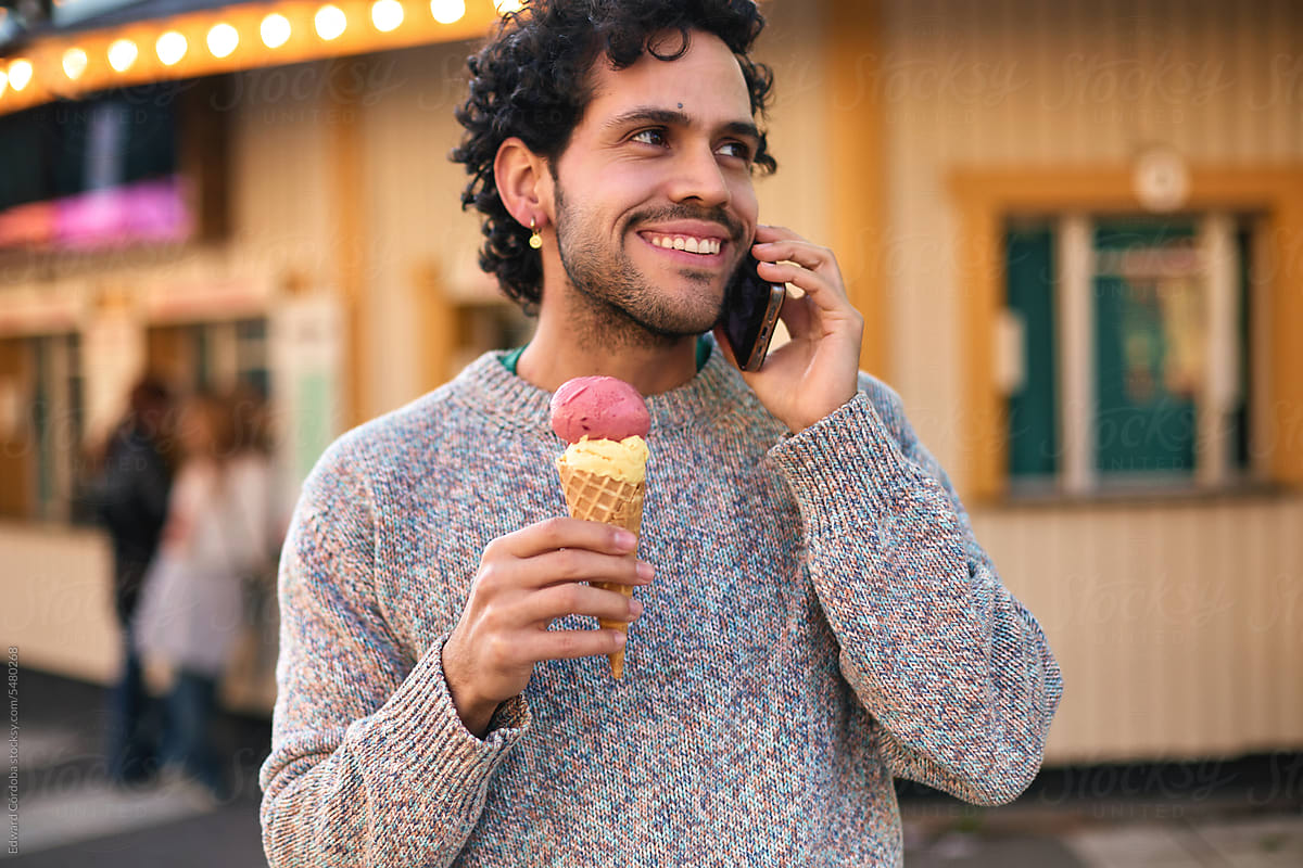 A young man speaks on his mobile phone while enjoying an ice cream.