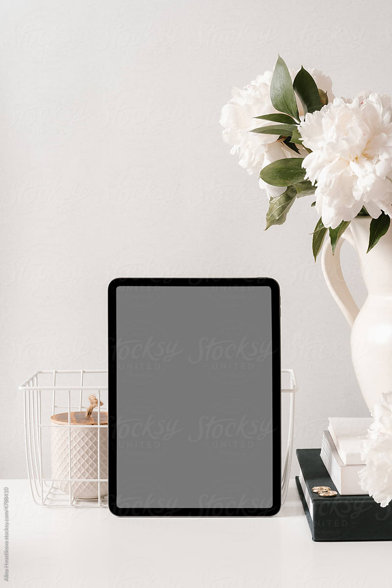 Tablet with flowers vase placed on table in light room