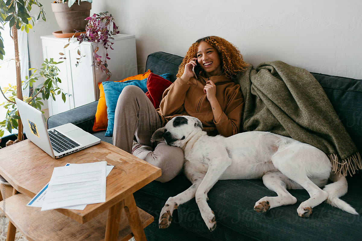 Young woman speaking on the phone on couch with dog