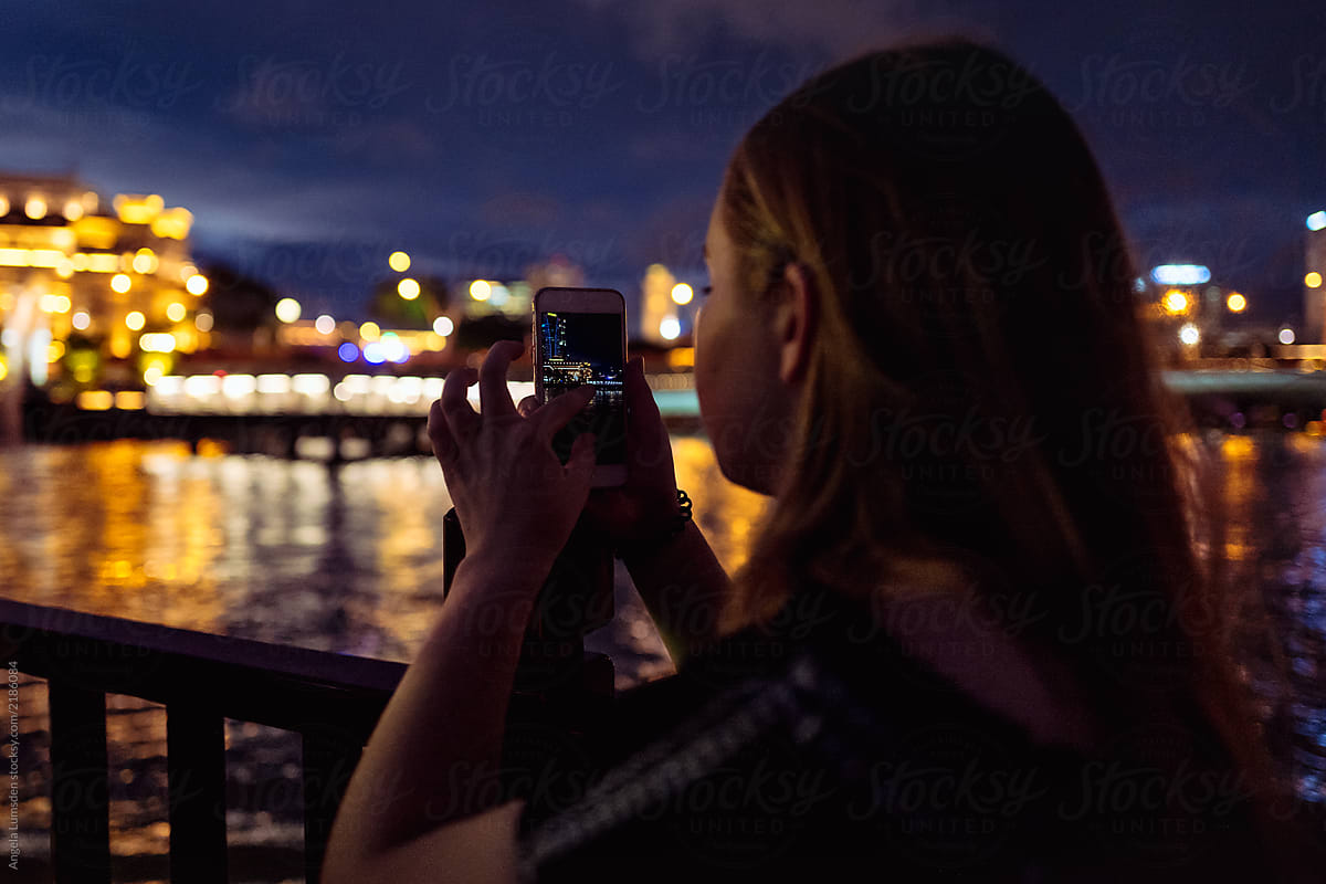Girl Taking A Photo Of Singapore&#39;s Merlion And Skyline At Night by Angela Lumsden
