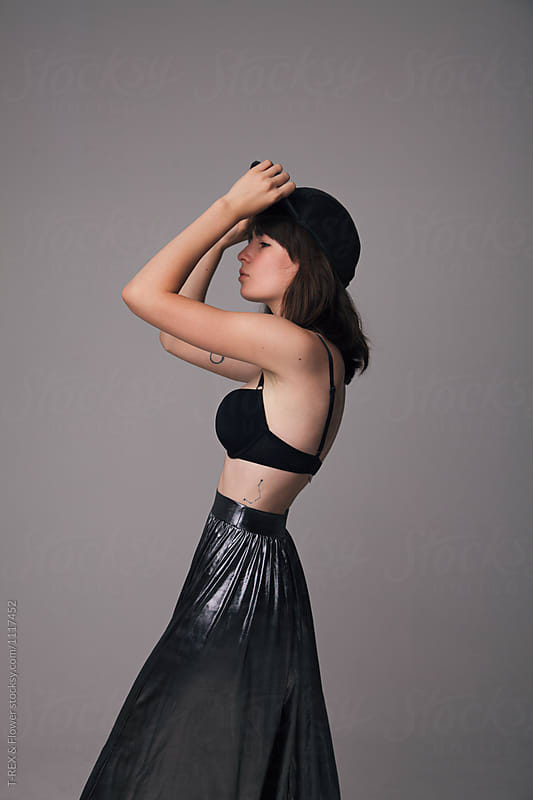 Girl in baseball cap,bra and metallic skirt ob grey wall