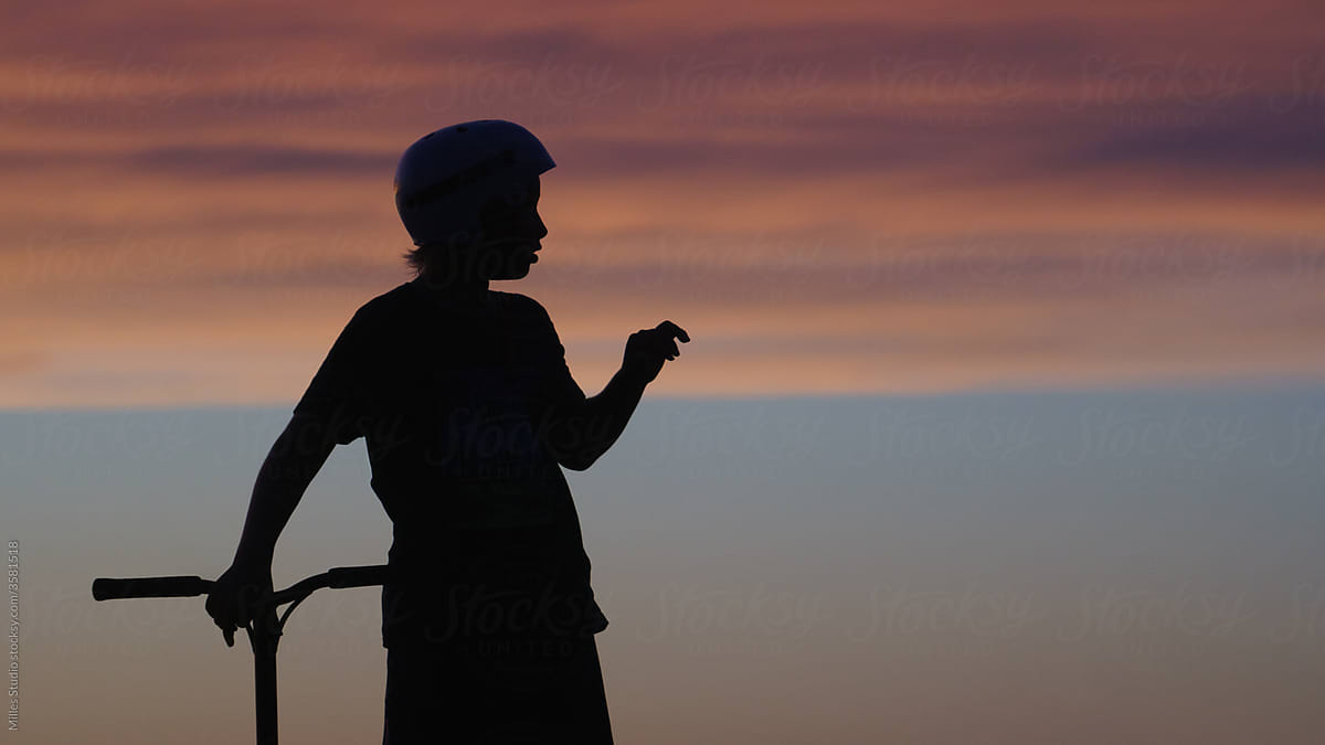 Boy with kick scooter against sundown sky