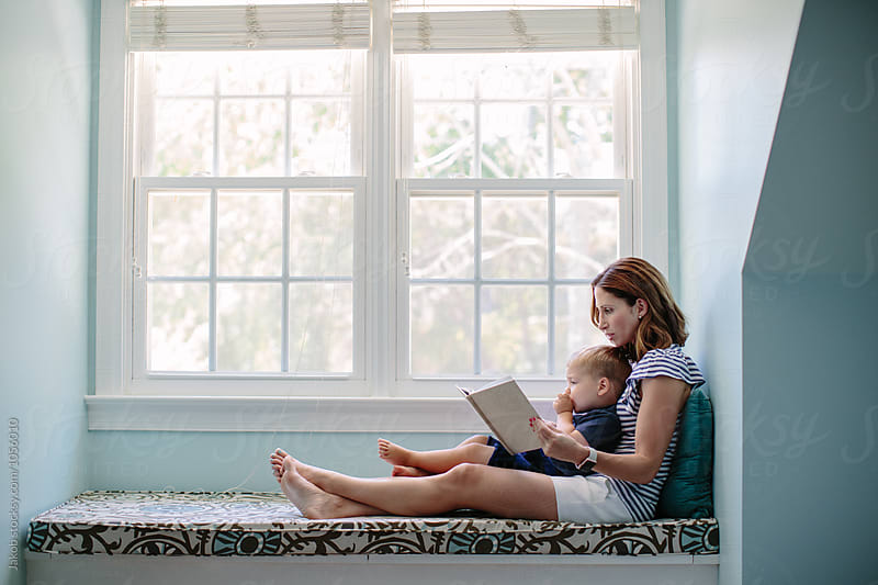Mother sitting on a window sill reading a book to her son