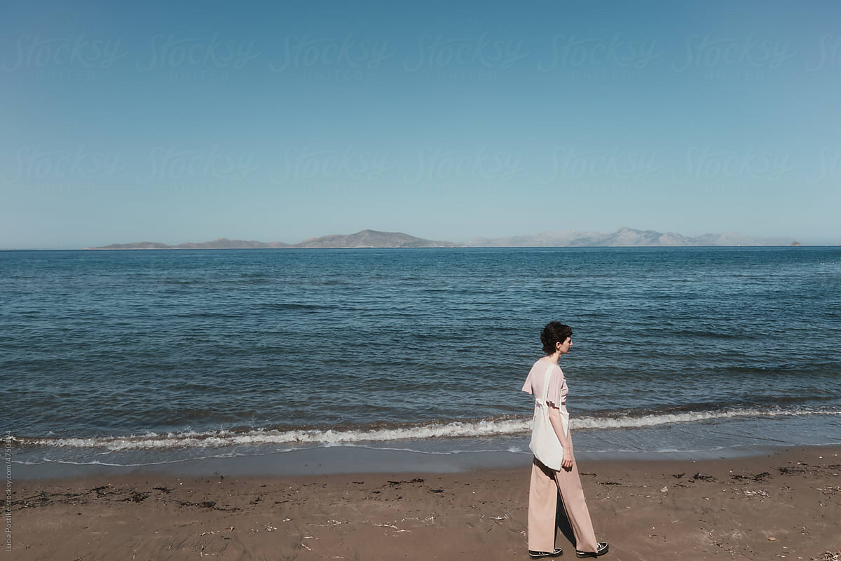 A woman in pink walks along the beach of the Aegean Sea.