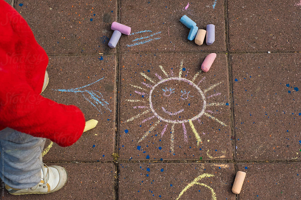 A child is drawing a smiling sun by chalk on a pavement