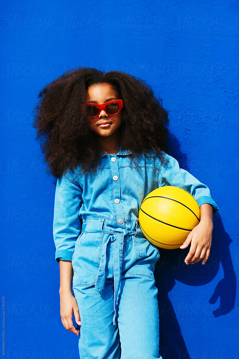 Fashionable African American girl with ball smiling and standing on street