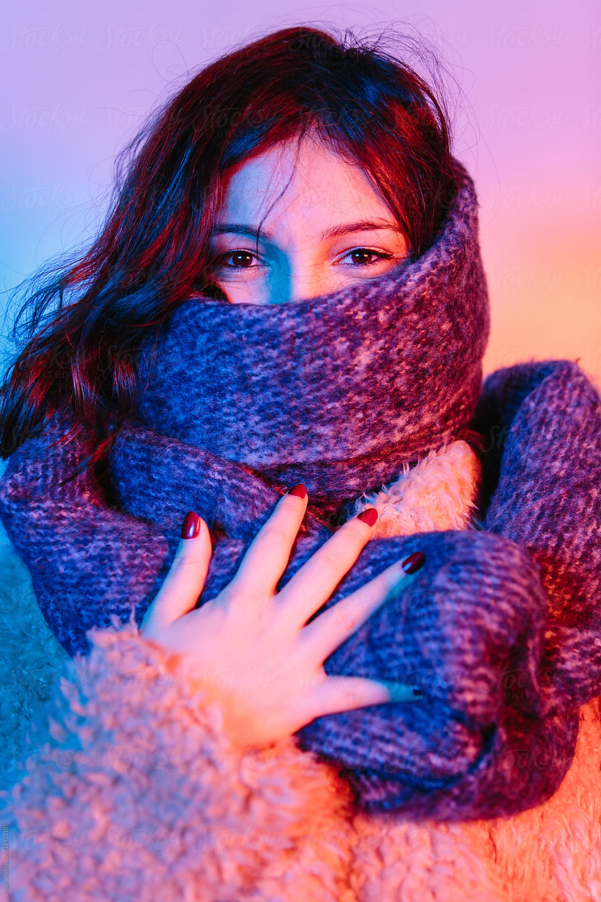 woman wearing winter clothing and big scarf with face partially covered with pink and blue lighting