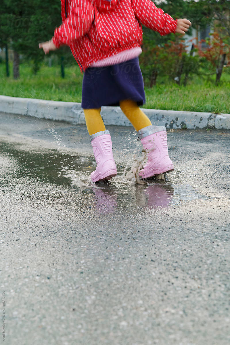 Anonymous kid jumping in puddle on road on rainy day
