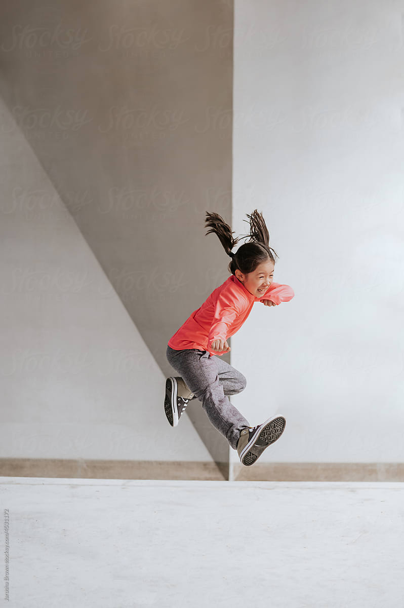 Young girl in workout clothes does a karate kick near a concrete wall.