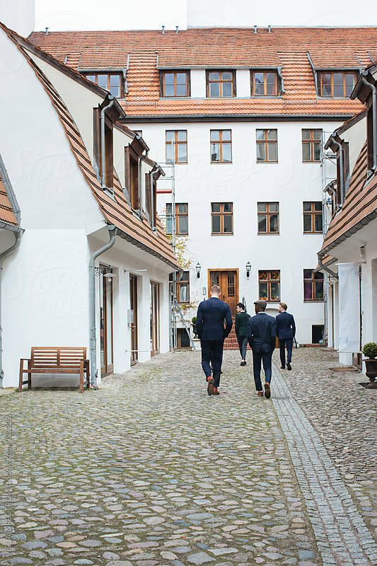 Five Stylish Young Men in Suits Walking in Courtyard From Behind