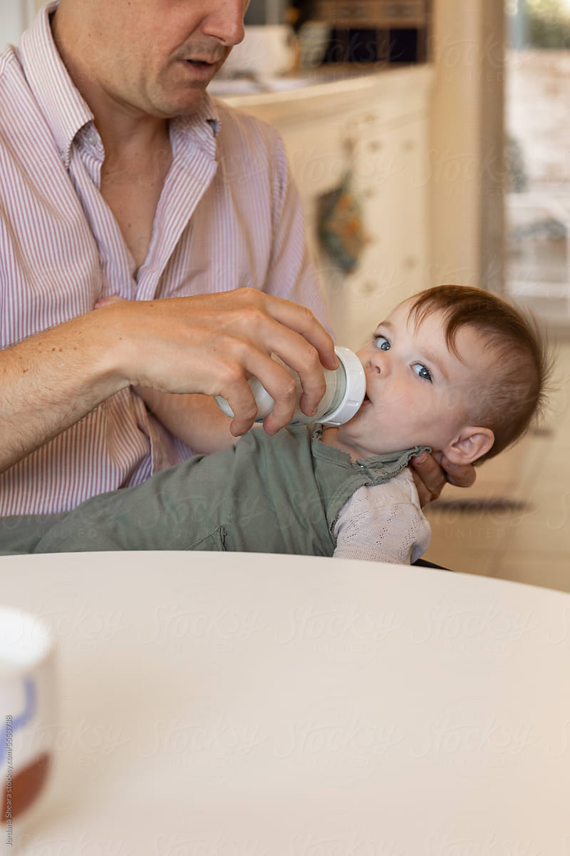 Father feeding baby daughter with bottle at home
