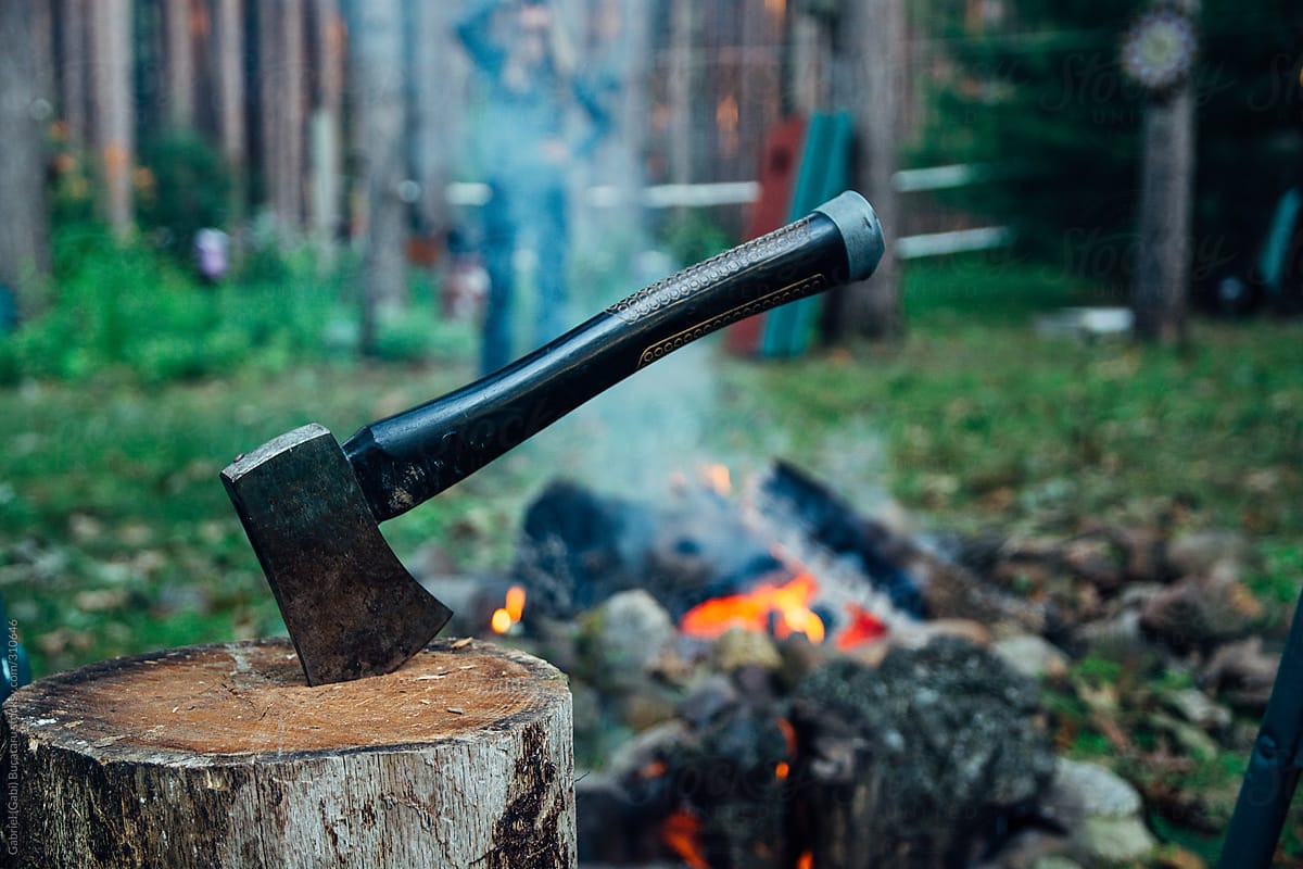 Small Hand Hatchet in a Wood Stump By A Lit Camping Fire in a Forest
