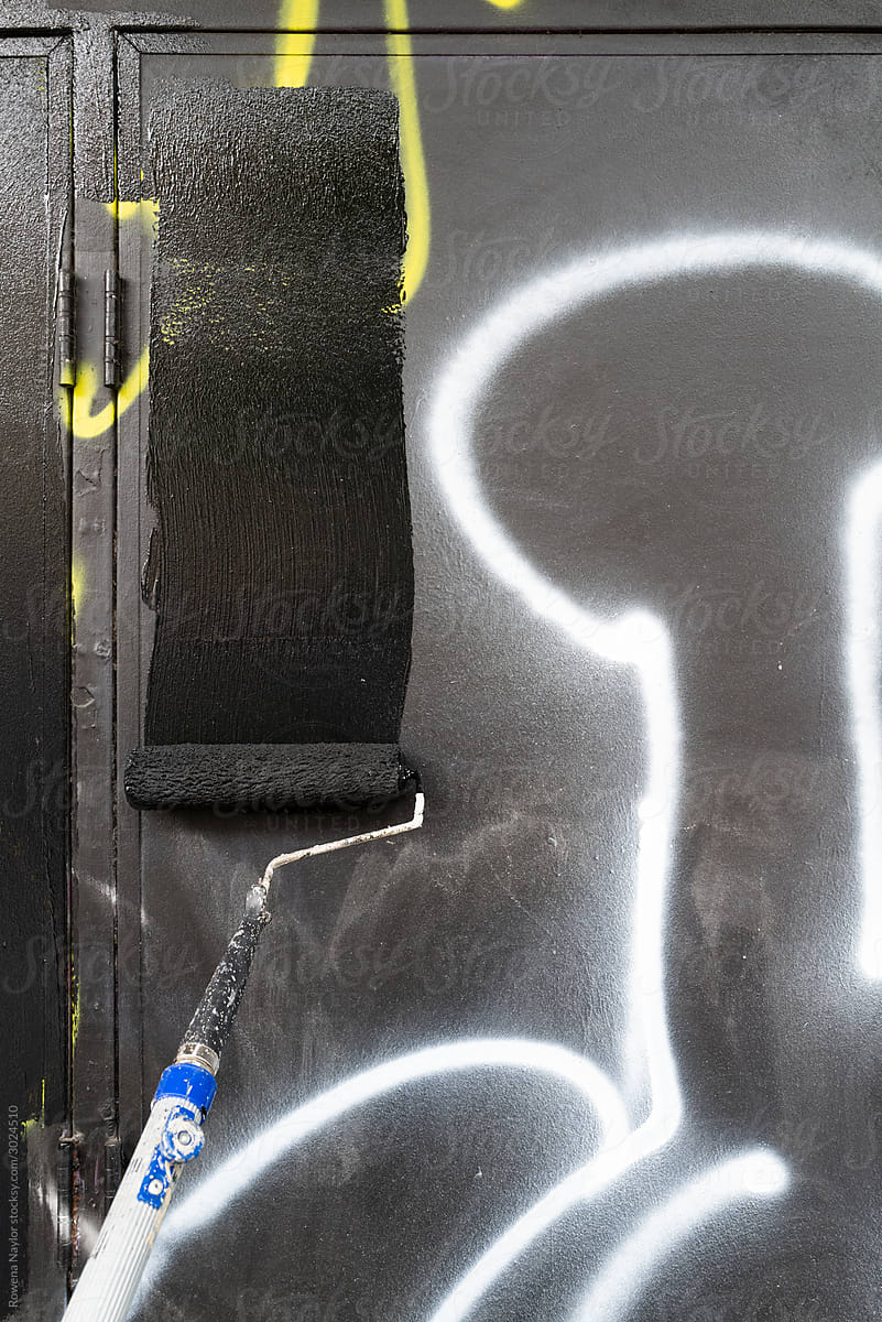 Council worker removing street graffiti by painting over with black paint