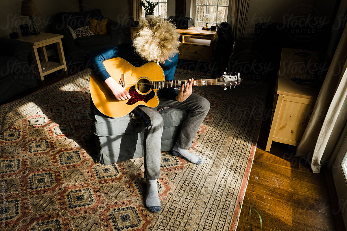 teen with blond curly hair playing guitar
