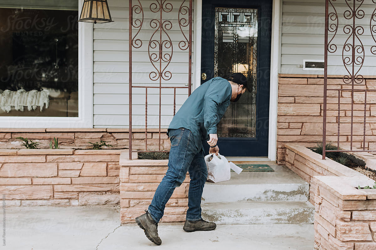 A Delivery Person Leans Forward to Drop Off a Food Delivery on a Home\'s Porch