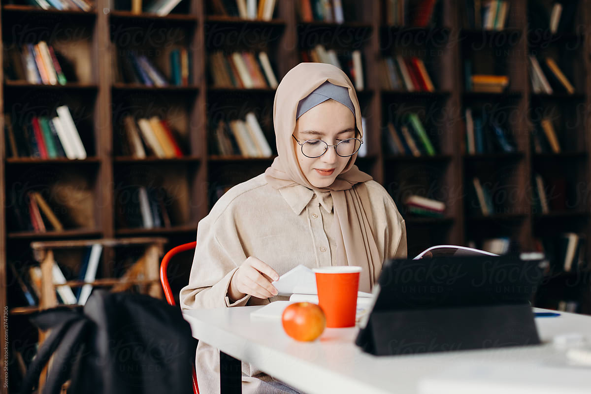 Cheerful Muslim female student  doing homework in library