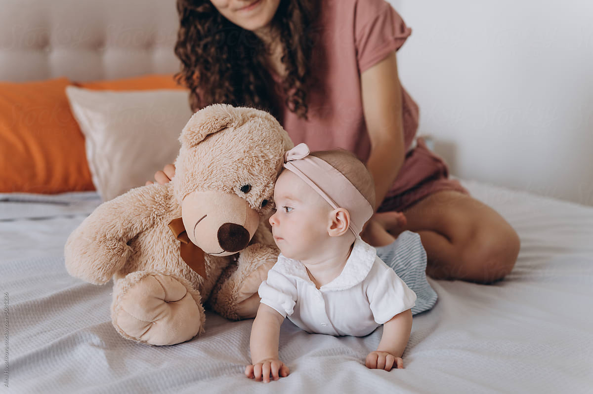 Mother playing with teddy bear and baby on bed