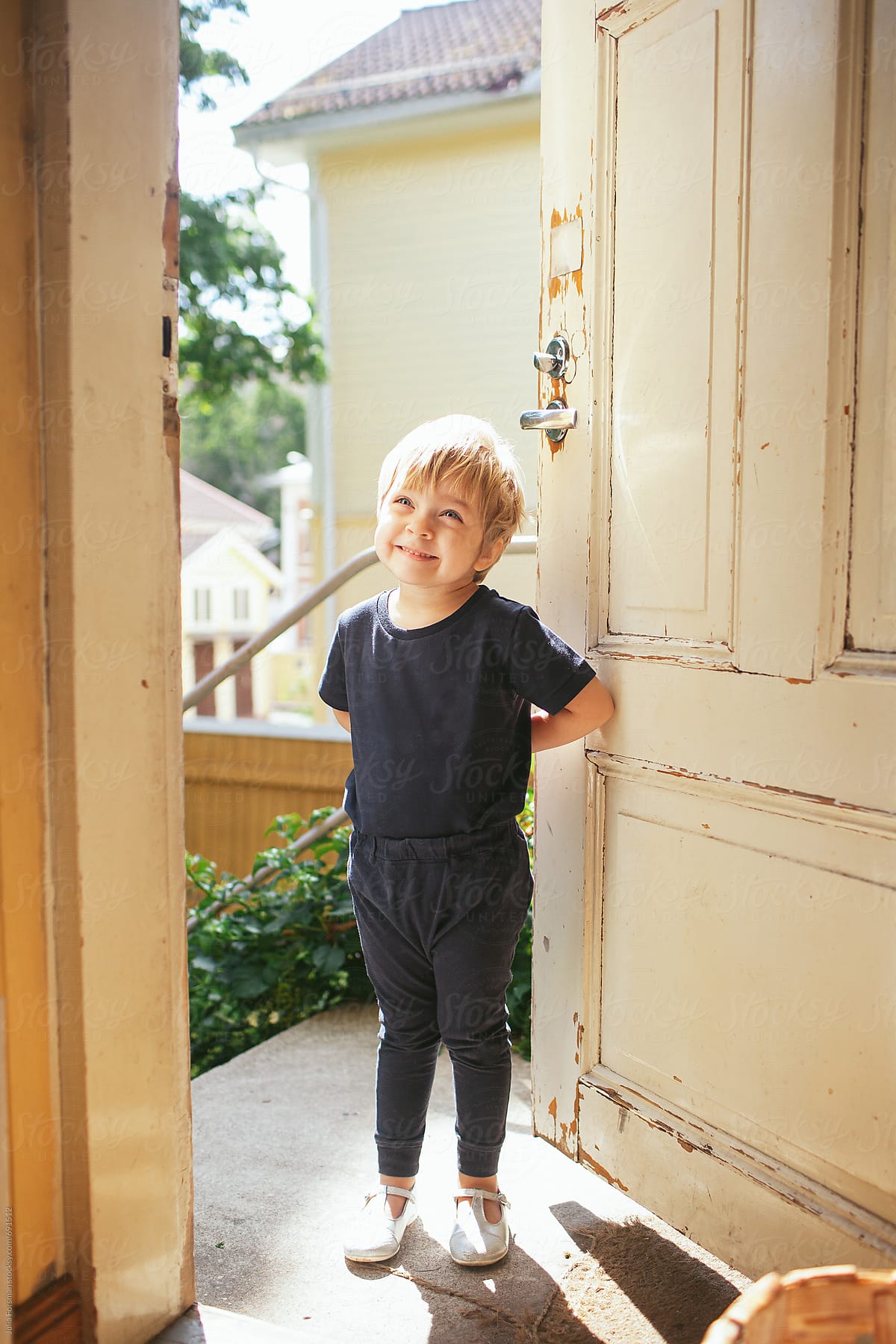Cute, happy little child saying hello at the front door of a house.