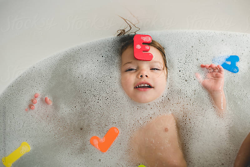Toddler girl playing with alpha letters in tub
