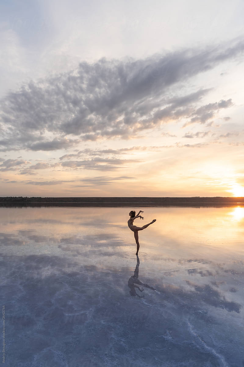 Female ballet dancer is posing in lagoon on low sun background
