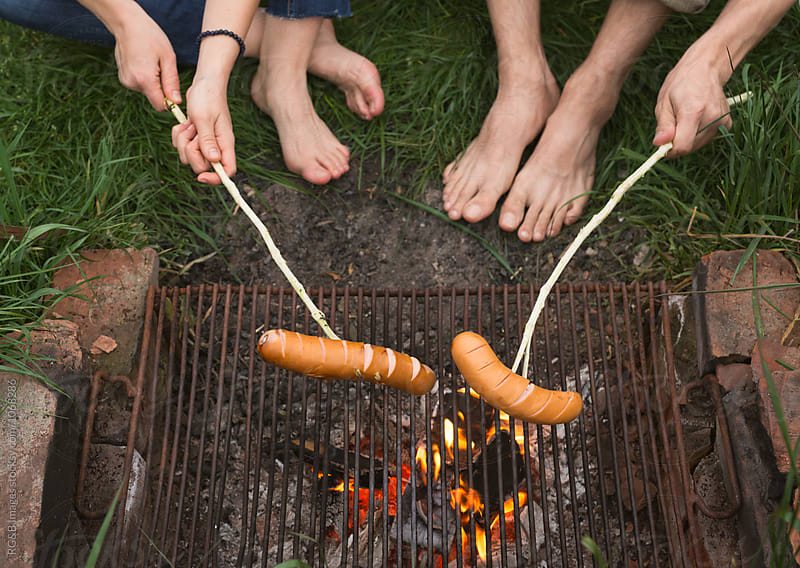 Young couple on vacation roasting sausages over camp fire
