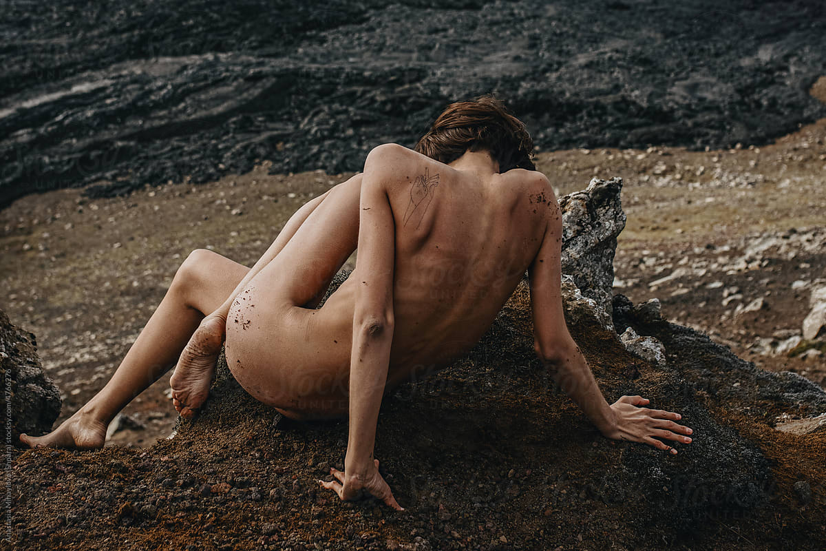 Naked woman sitting in front of black lava river in Iceland