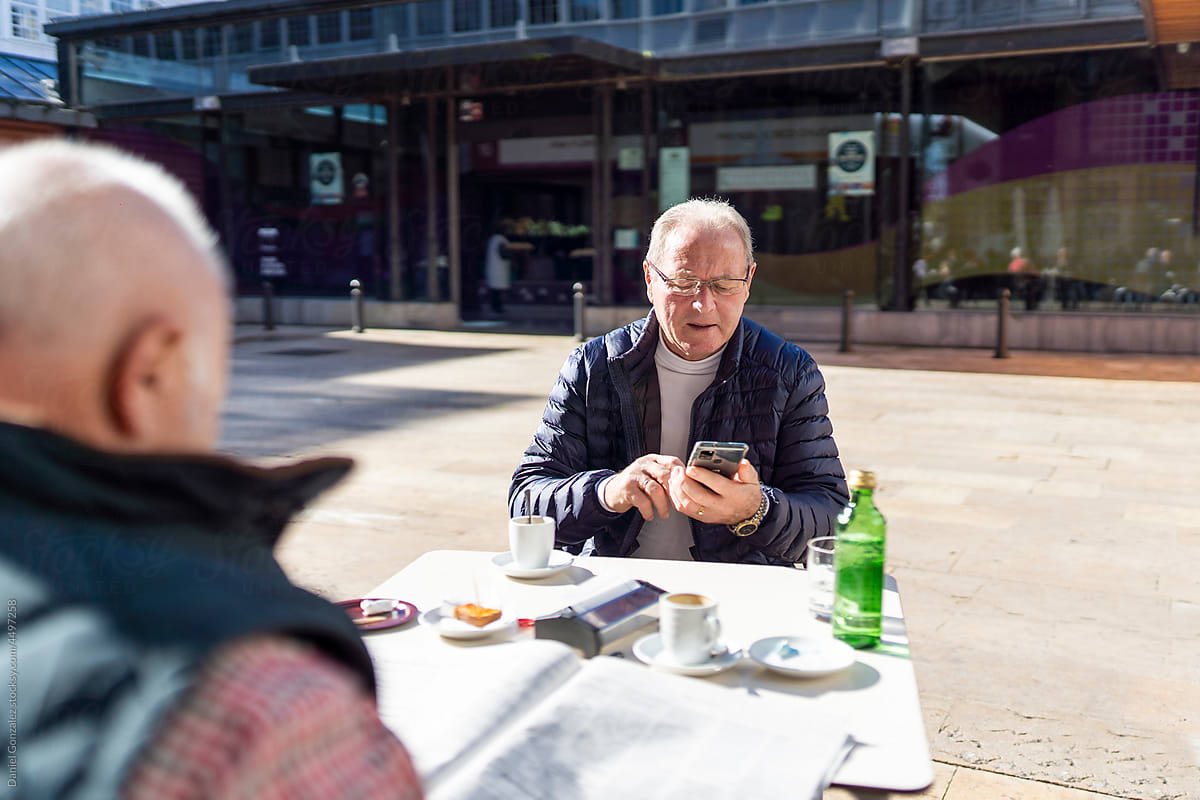 Pensioner using smartphone near friend in cafe