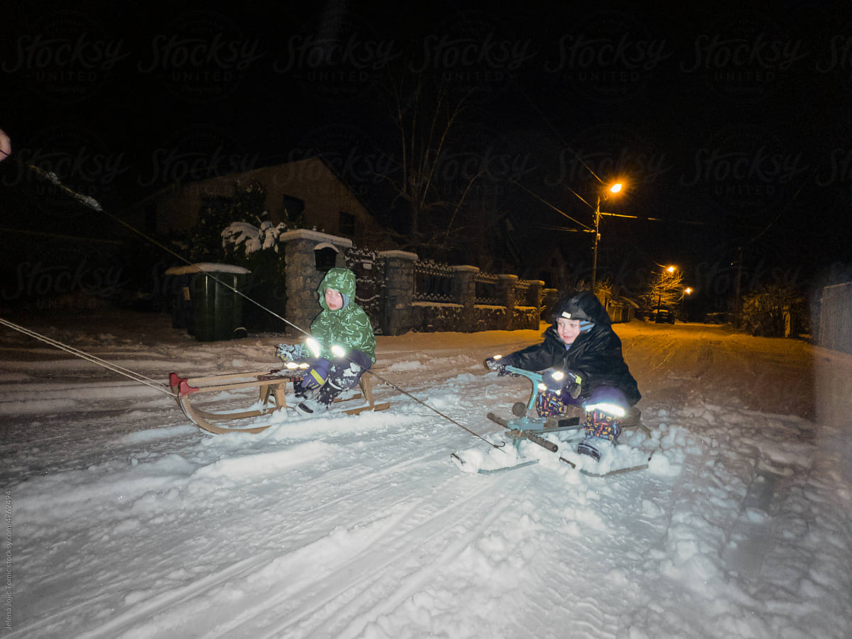 Fast snow night ride of two boys on sleds