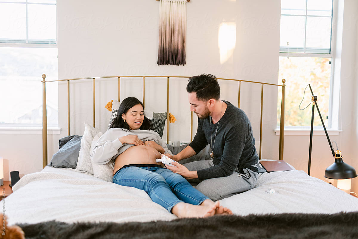 Pregnant mother and father testing fetal monitor in bed