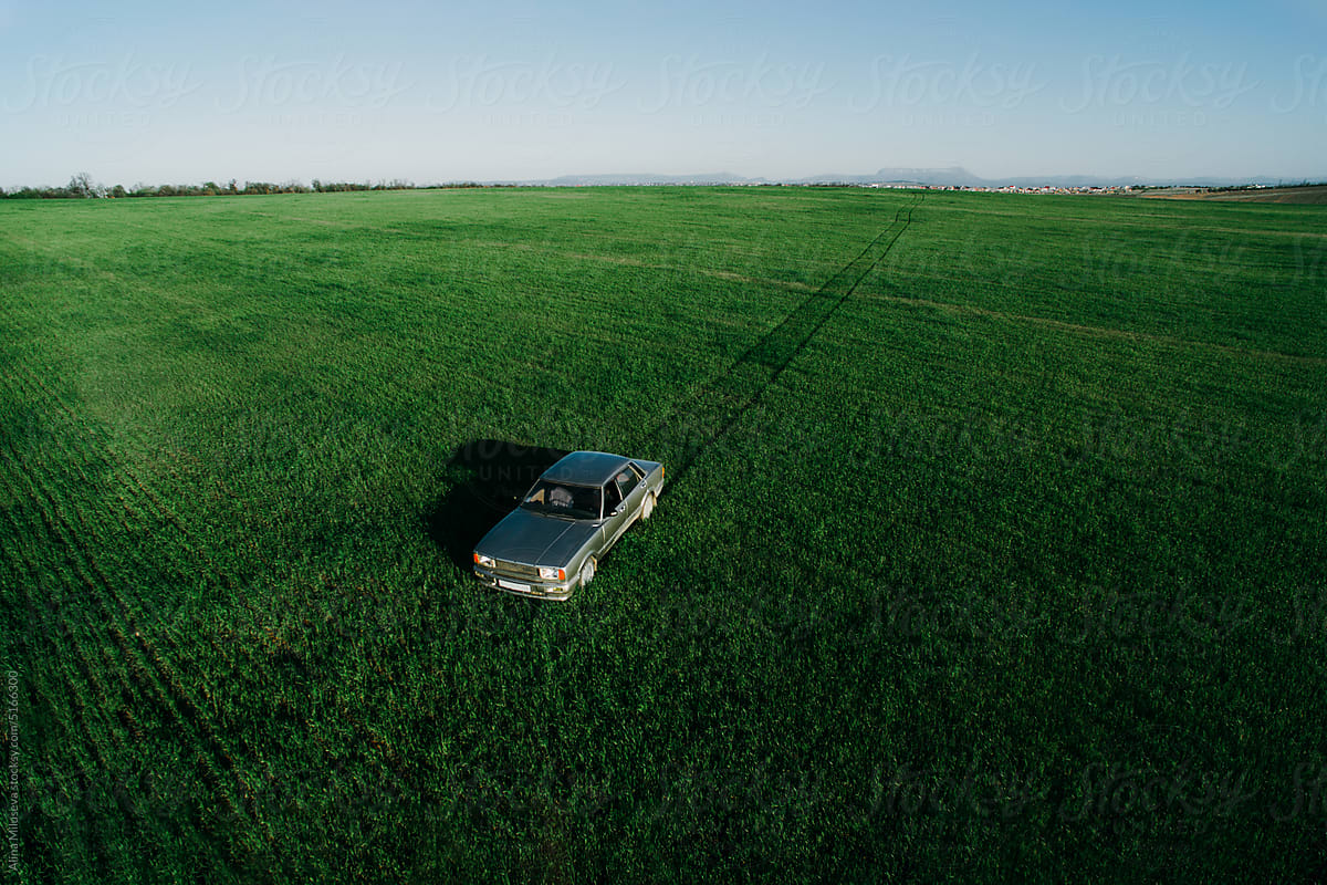 Car driving on green farmland, leaving traces on field