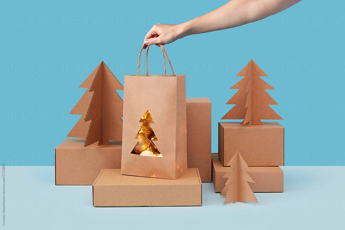 Female hand putting papercraft bag with christmas decor on gift boxes