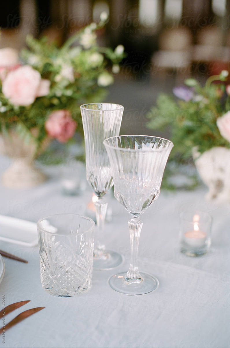 Crystal glassware sits atop a linen tablecloth decorated with accents of greenery and florals
