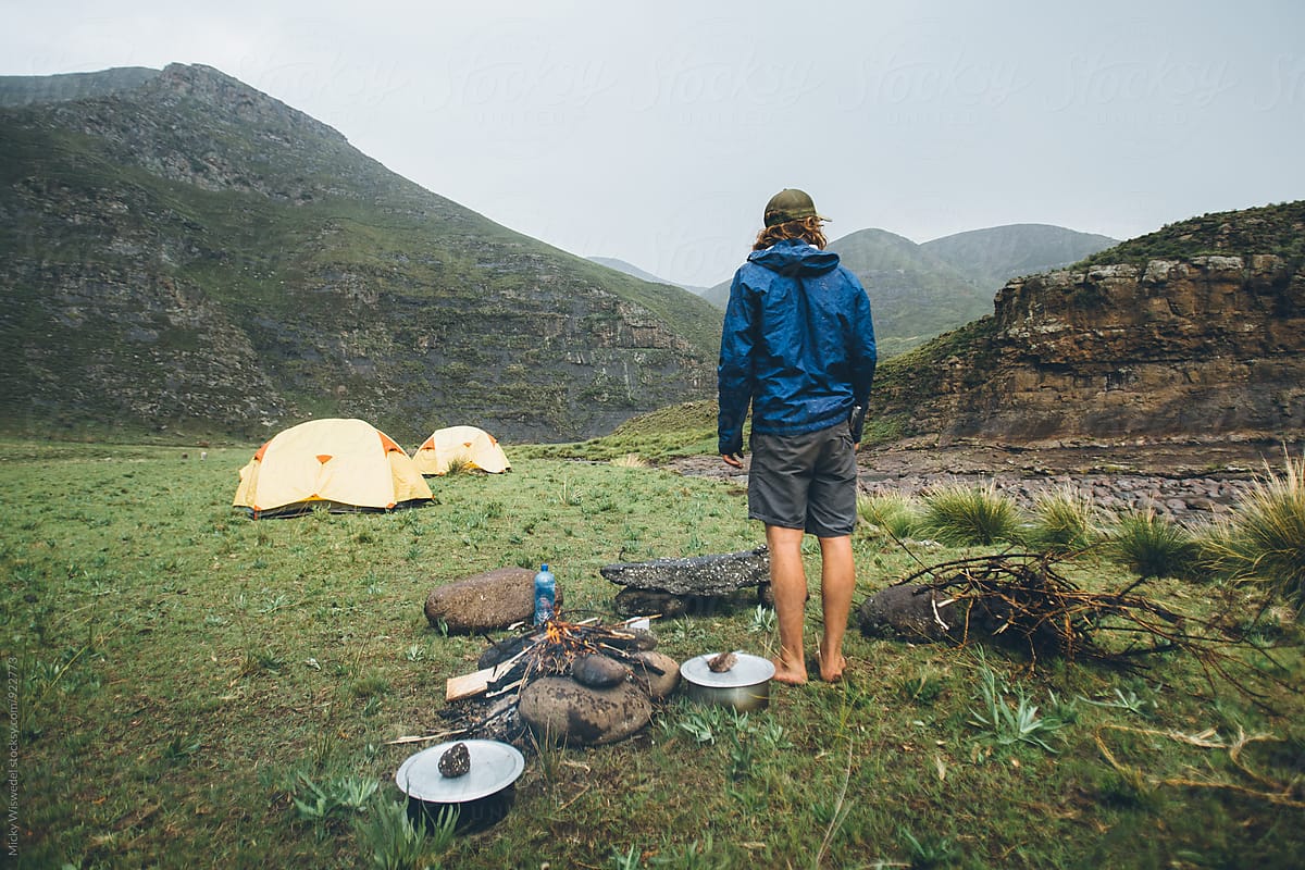 hiker outdoorsman standing by a campfire in camp on a rainy day in the mountains
